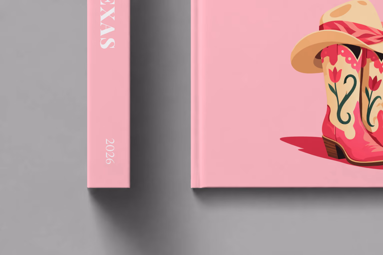 Texas hardcover photo book with the illustrated cover of pink cowboy boots and a cowboy hat with a pink bandana on pink, shown close up beside its spine on a pale grey studio surface