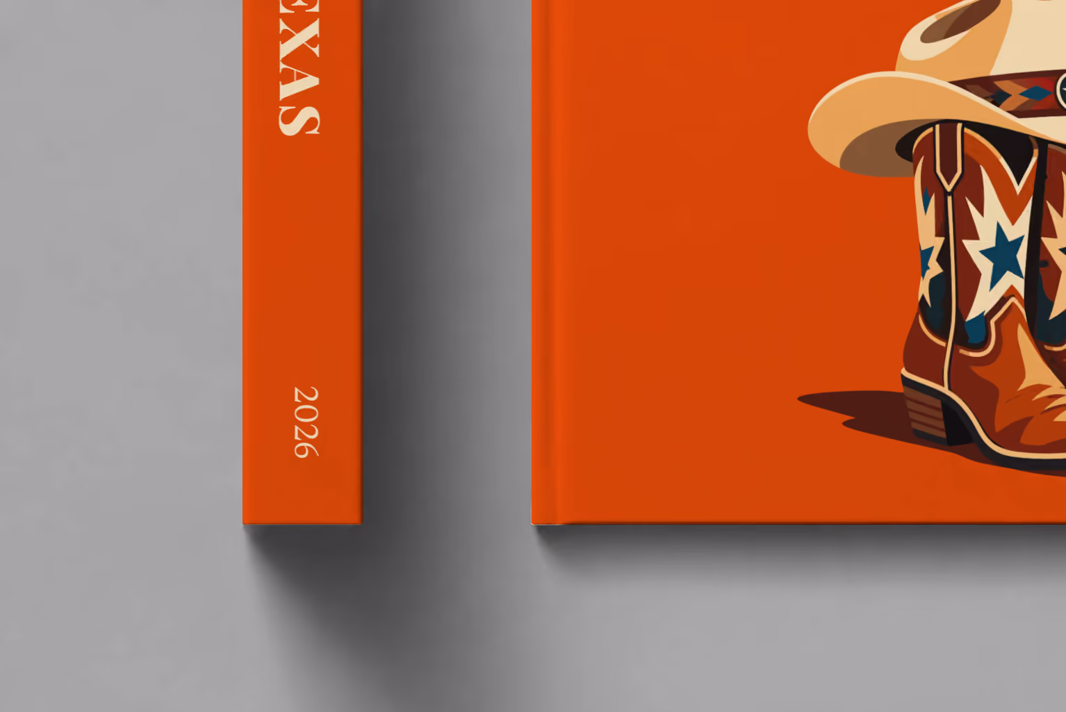 Texas hardcover photo book with the illustrated cover of cowboy boots with blue stars and a cowboy hat on burnt orange, shown close up beside its spine on a pale grey studio surface