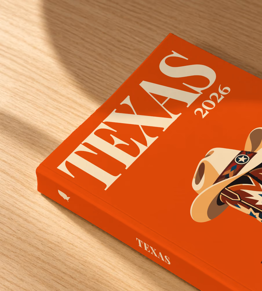 Texas softcover photo book with the illustrated cover of cowboy boots with blue stars and a cowboy hat on burnt orange, lying on an oak desk in dappled afternoon sunlight