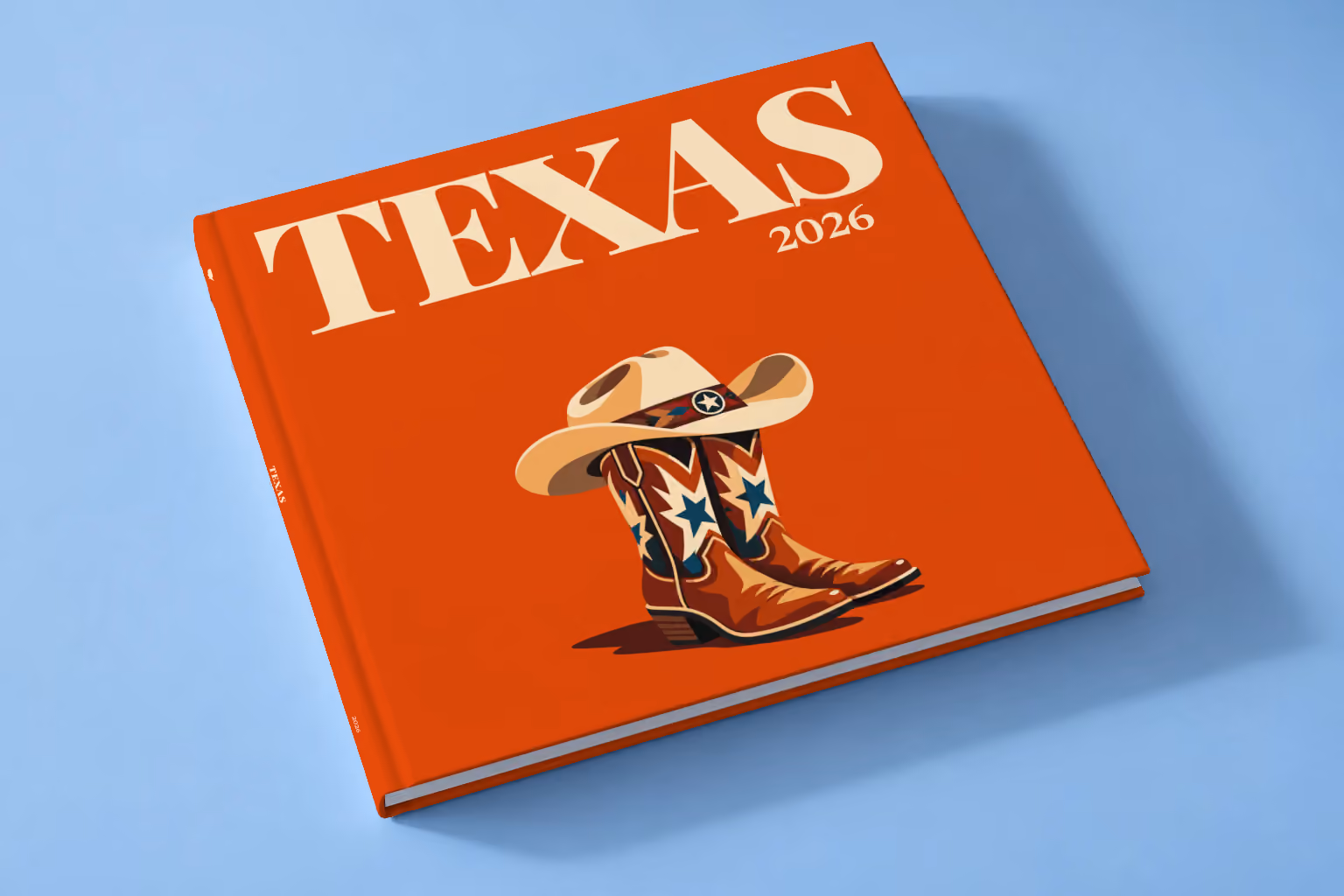 Texas square hardcover photo book with the illustrated cover of cowboy boots with blue stars and a cowboy hat on burnt orange, lying on a pale blue studio backdrop