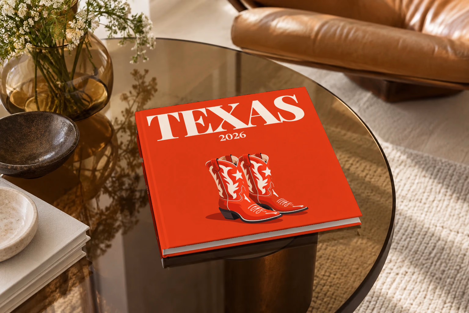 Texas square hardcover photo book with the illustrated cover of a pair of red cowboy boots with white stars on red, on a smoked glass coffee table beside a leather armchair in warm afternoon light