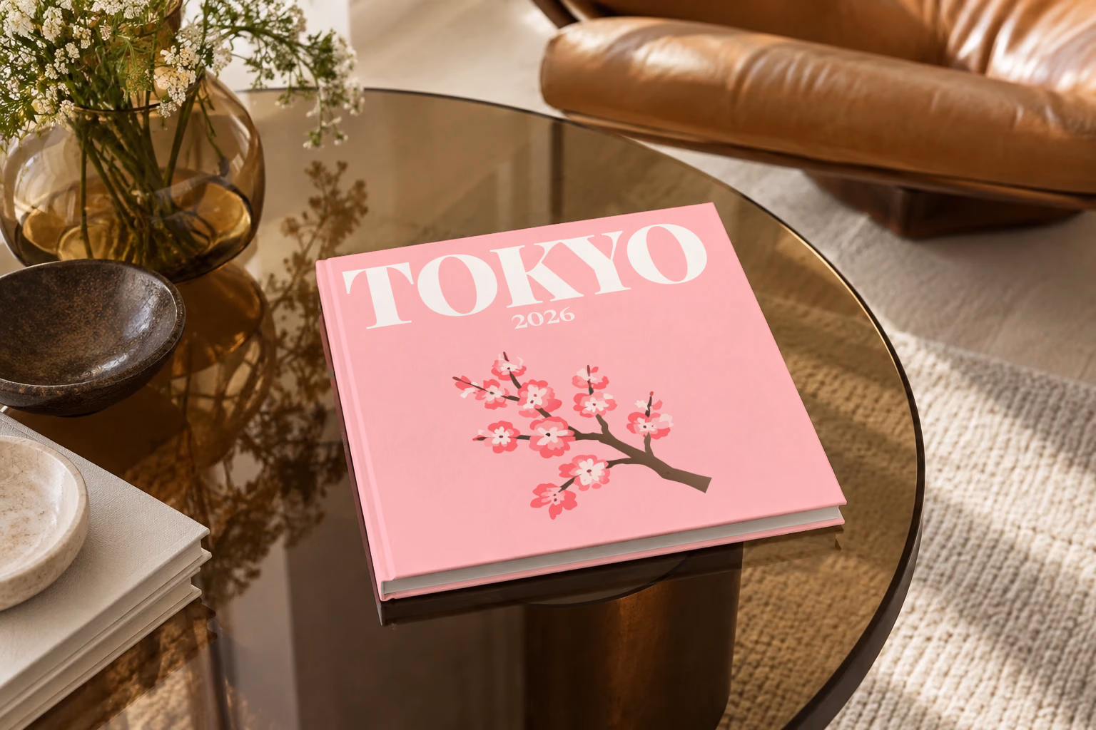 Tokyo square hardcover photo book with the illustrated cover of a cherry blossom branch on pink, on a smoked glass coffee table beside a leather armchair in warm afternoon light