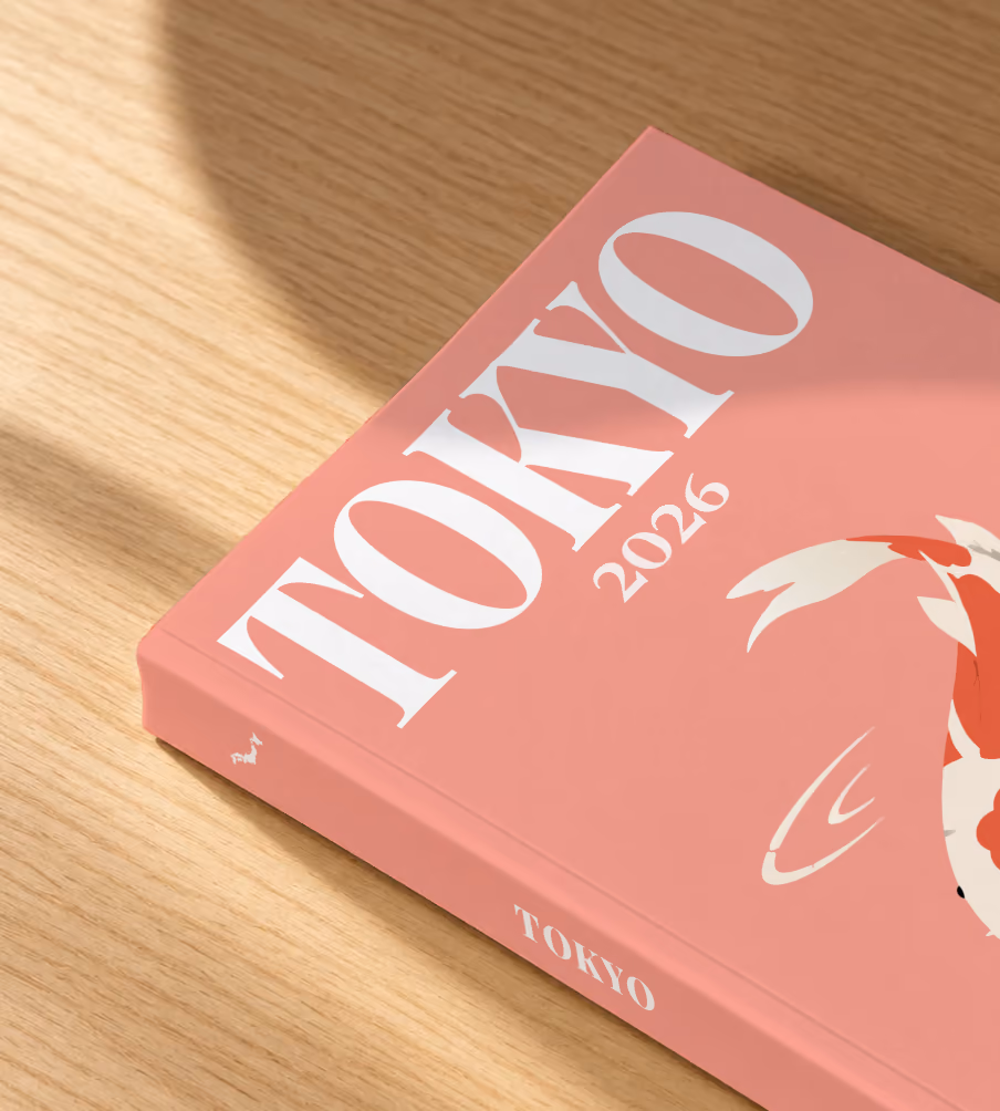 Tokyo softcover photo book with the illustrated cover of a koi on coral pink, lying on an oak desk in dappled afternoon sunlight