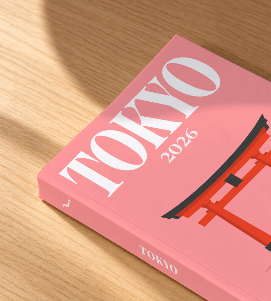 Tokyo softcover photo book with the illustrated cover of a red torii gate and petals on pink, lying on an oak desk in dappled afternoon sunlight