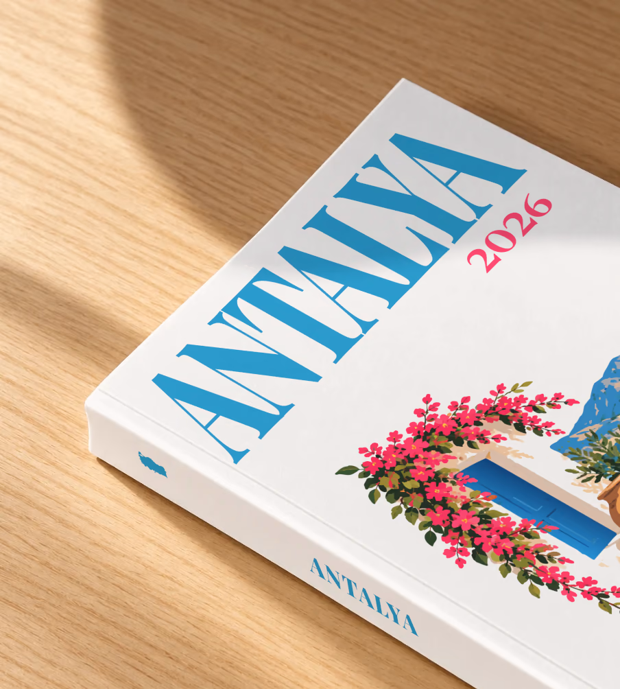 Turkey softcover photo book with the Antalya illustrated cover of a blue door draped in pink bougainvillea above the Antalya coast on white, lying on an oak desk in dappled afternoon sunlight