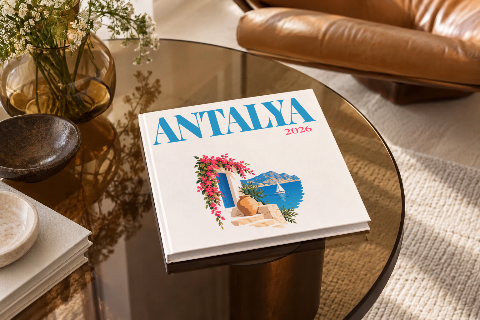 Turkey square hardcover photo book with the Antalya illustrated cover of a blue door draped in pink bougainvillea above the Antalya coast on white, on a smoked glass coffee table beside a leather armchair in warm afternoon light