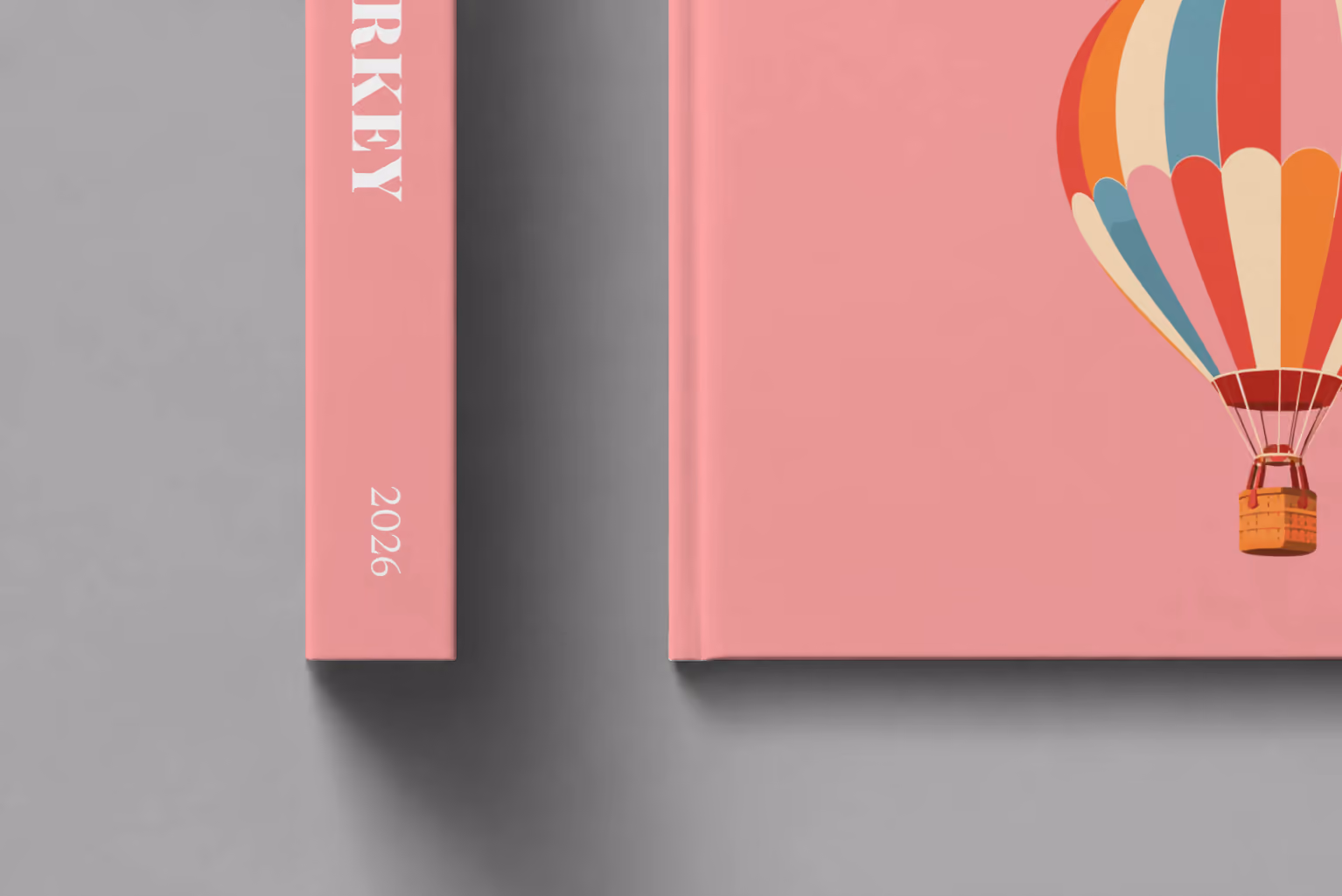 Turkey hardcover photo book with the illustrated cover of a striped Cappadocia hot air balloon on pink, shown close up beside its spine on a pale grey studio surface