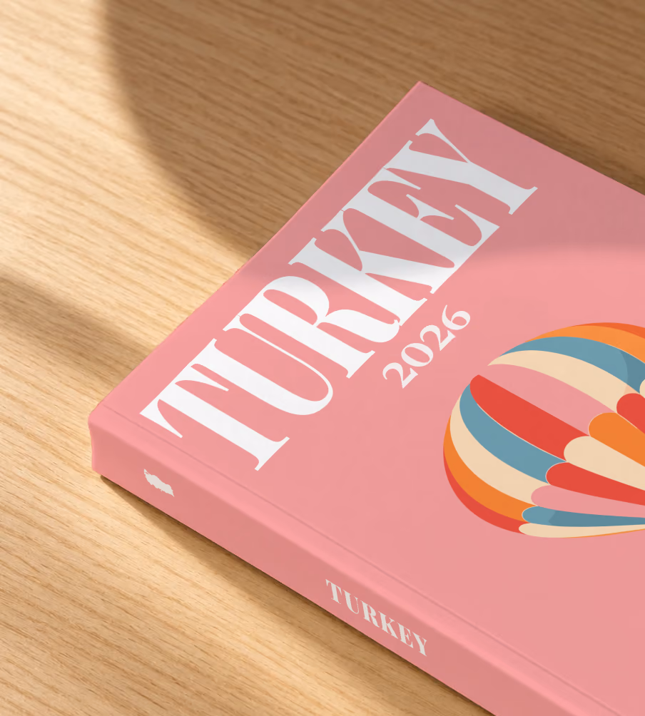 Turkey softcover photo book with the illustrated cover of a striped Cappadocia hot air balloon on pink, lying on an oak desk in dappled afternoon sunlight