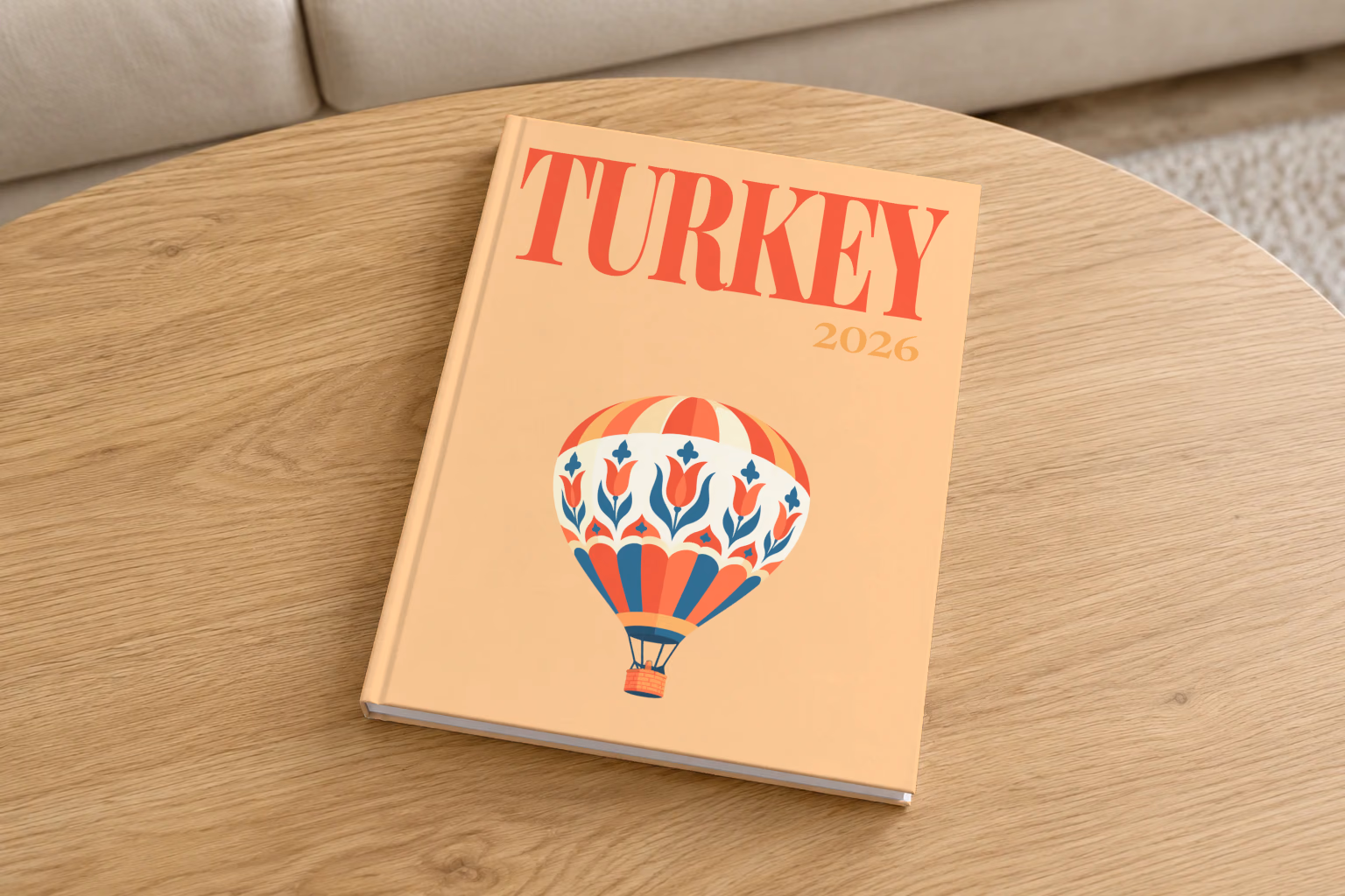 Turkey hardcover photo book with the illustrated cover of a hot air balloon patterned with Turkish tulips on peach, on a round oak coffee table in a bright living room