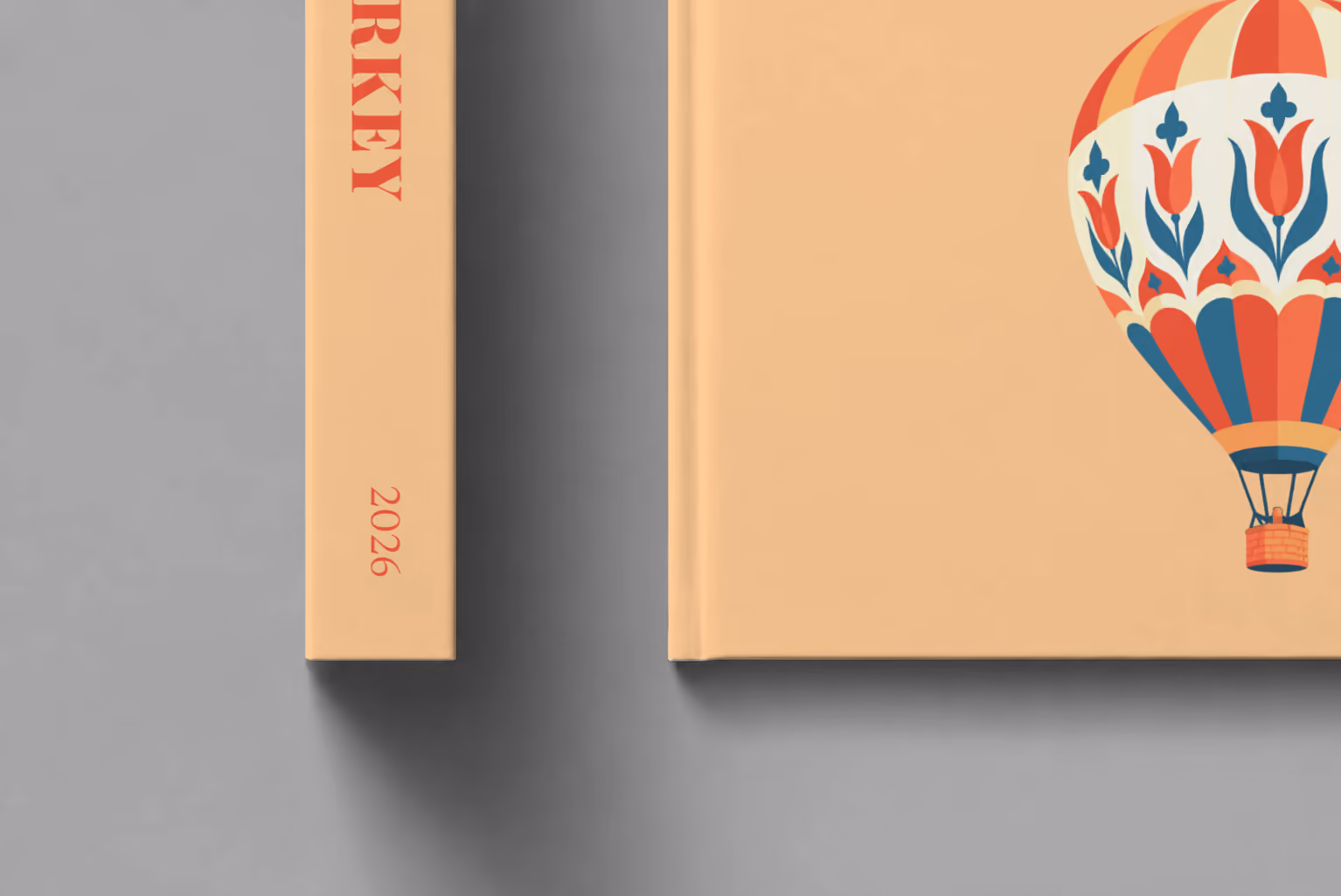 Turkey hardcover photo book with the illustrated cover of a hot air balloon patterned with Turkish tulips on peach, shown close up beside its spine on a pale grey studio surface