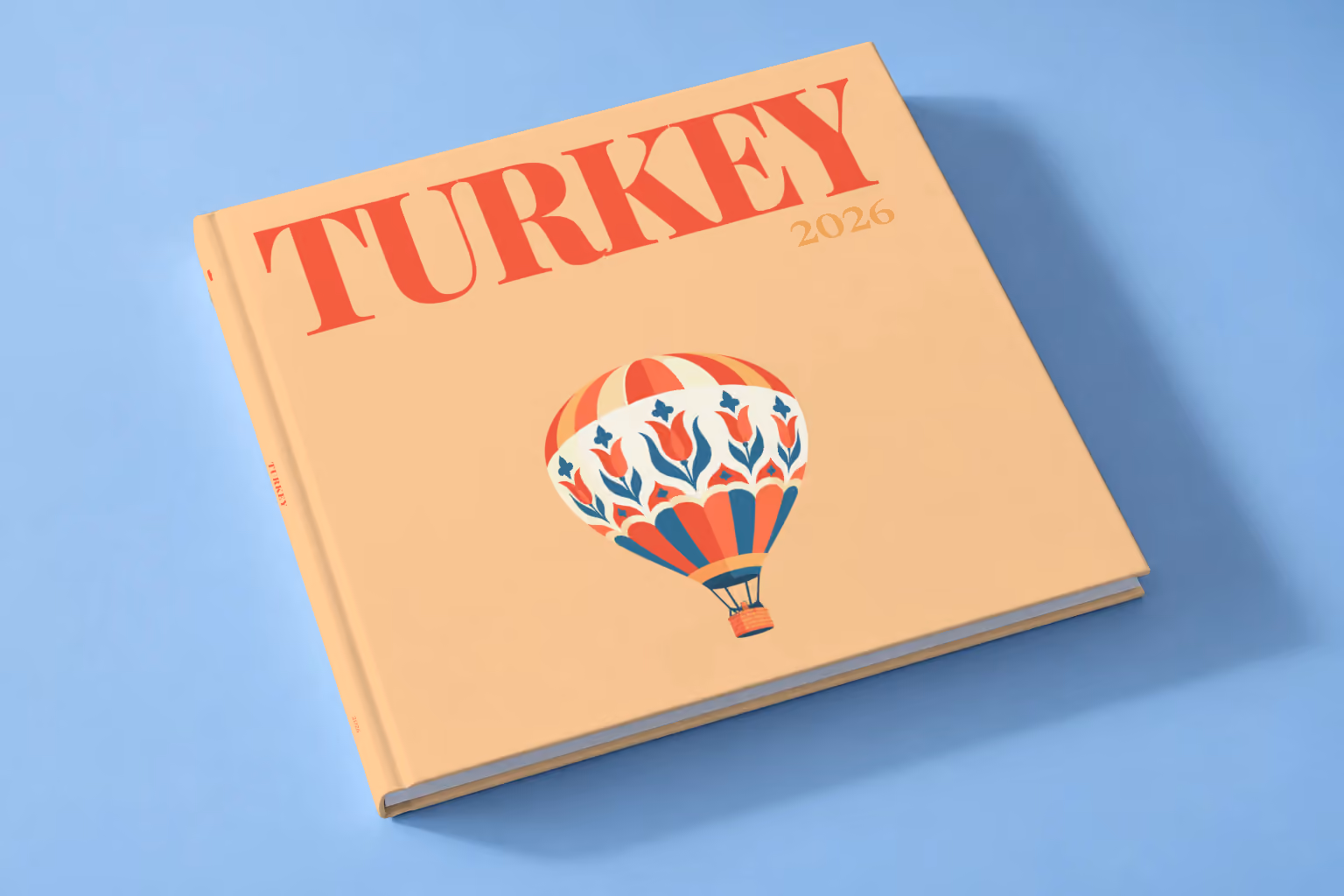 Turkey square hardcover photo book with the illustrated cover of a hot air balloon patterned with Turkish tulips on peach, lying on a pale blue studio backdrop