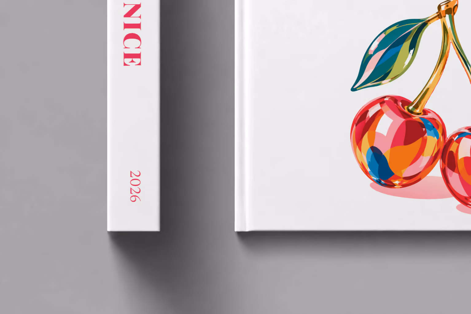 Venice hardcover photo book with the illustrated cover of glass cherries on white, shown close up beside its spine on a pale grey studio surface