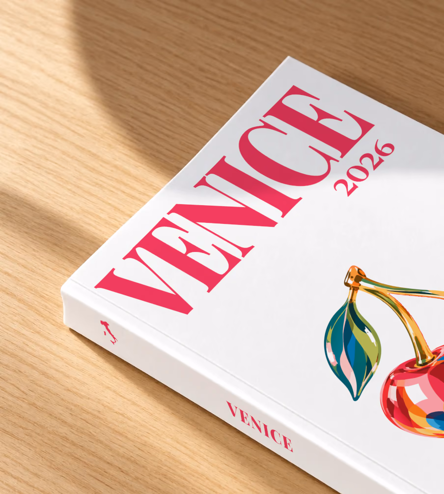 Venice softcover photo book with the illustrated cover of glass cherries on white, lying on an oak desk in dappled afternoon sunlight