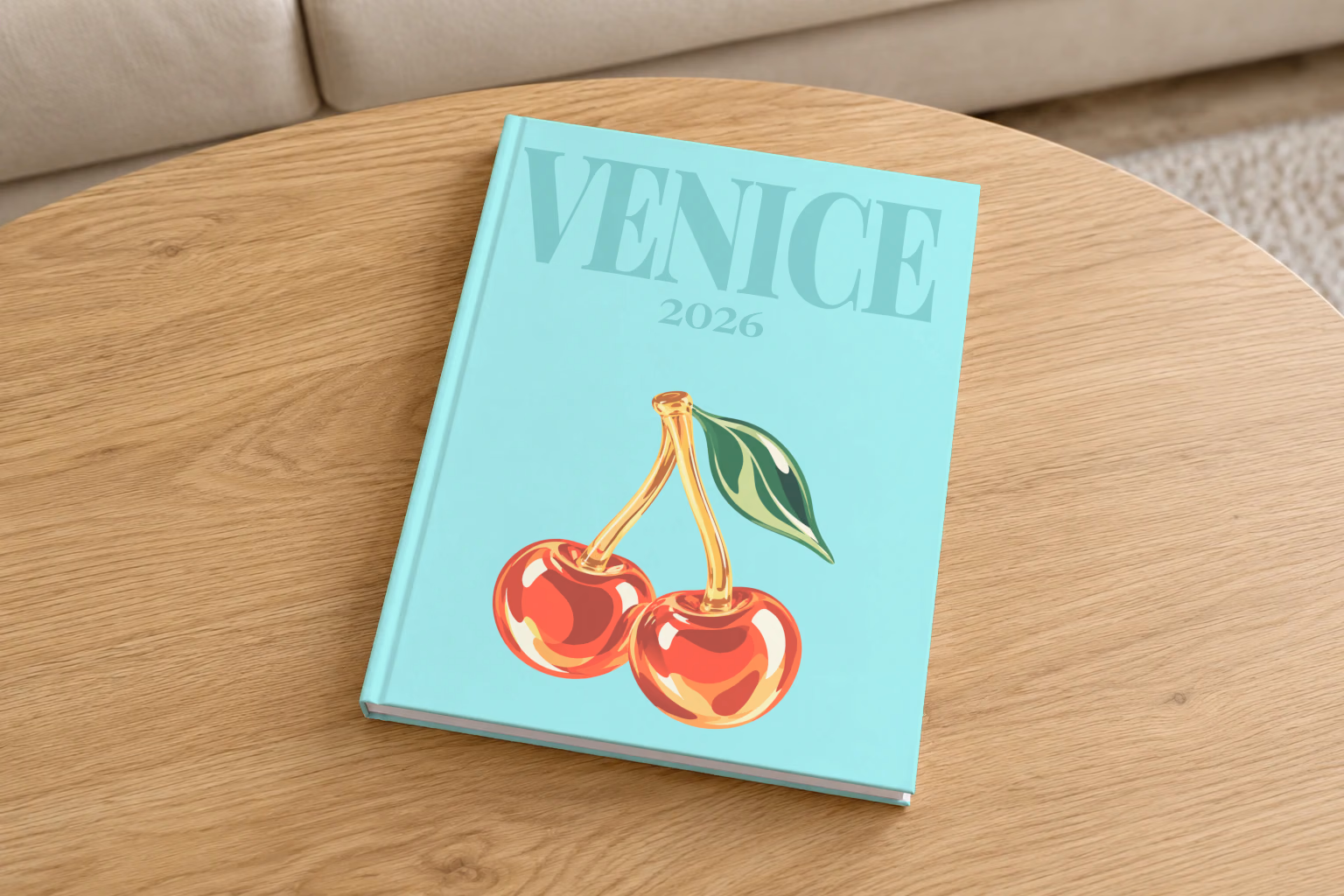 Venice hardcover photo book with the illustrated cover of glass cherries on pale aqua, on a round oak coffee table in a bright living room