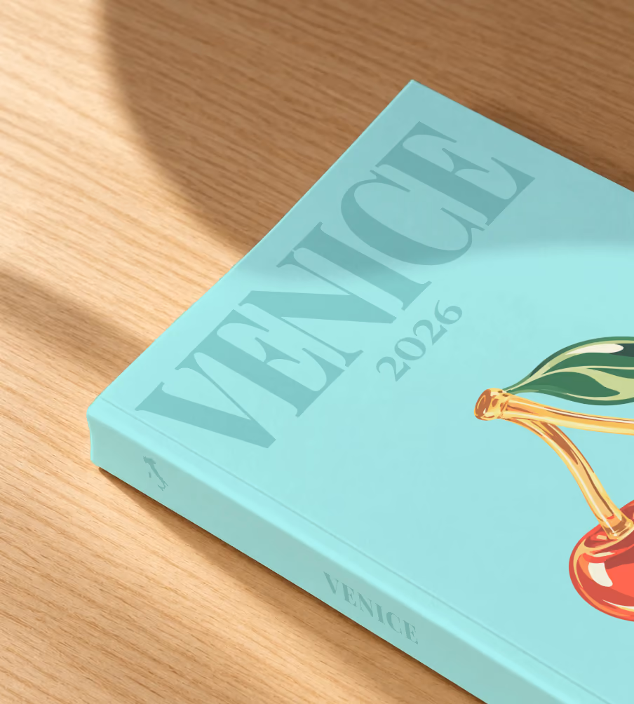 Venice softcover photo book with the illustrated cover of glass cherries on pale aqua, lying on an oak desk in dappled afternoon sunlight