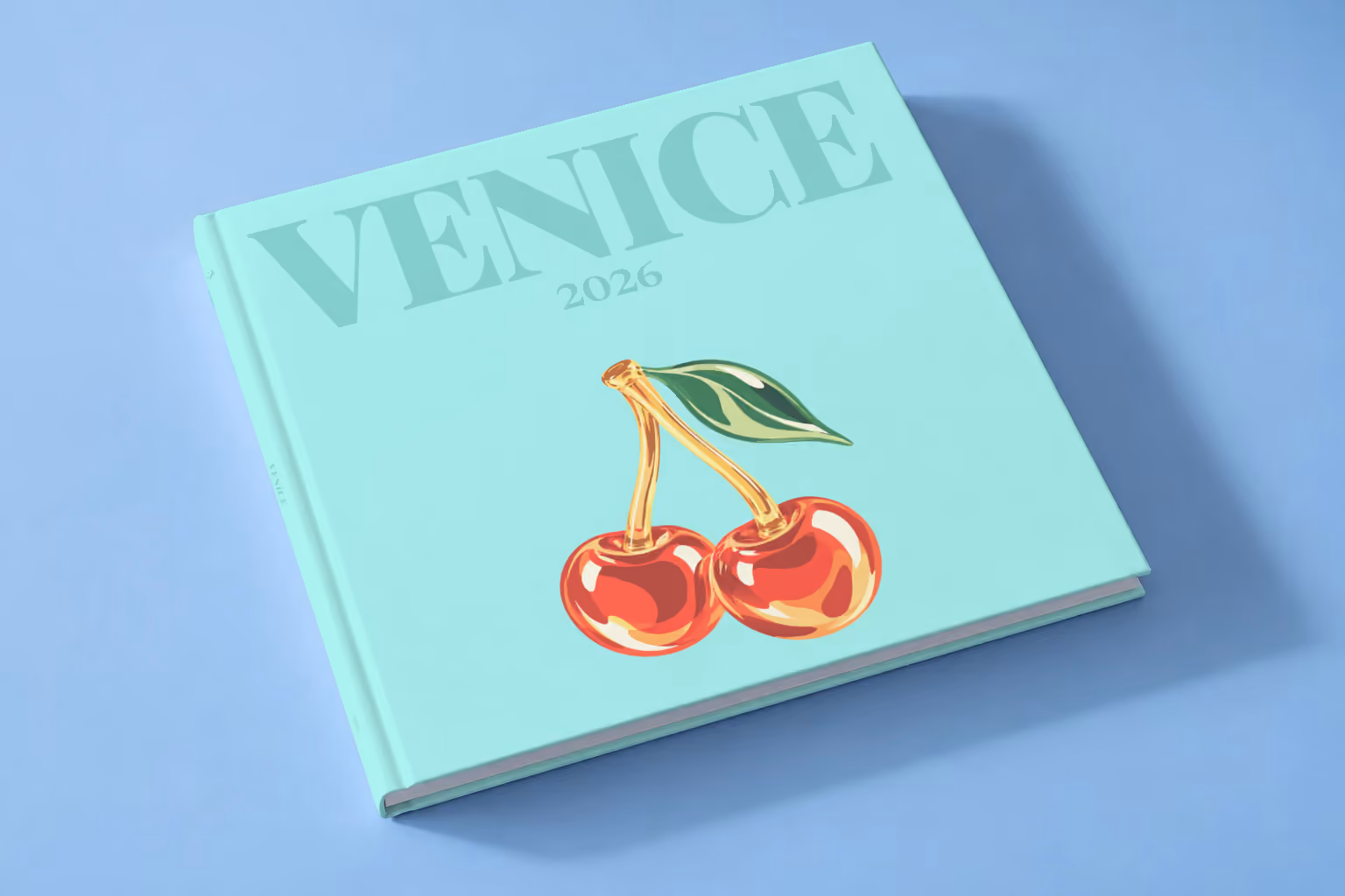 Venice square hardcover photo book with the illustrated cover of glass cherries on pale aqua, lying on a pale blue studio backdrop