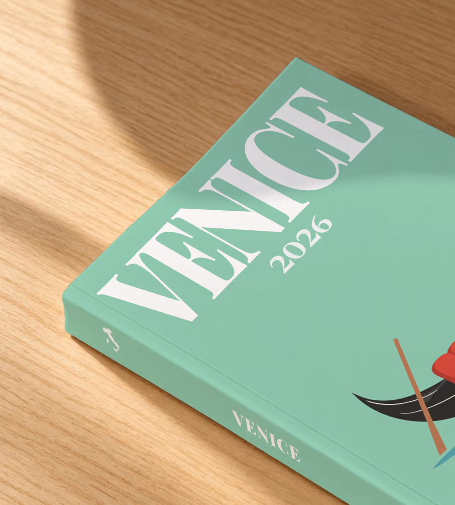 Venice softcover photo book with the illustrated cover of a gondola on the lagoon on mint green, lying on an oak desk in dappled afternoon sunlight