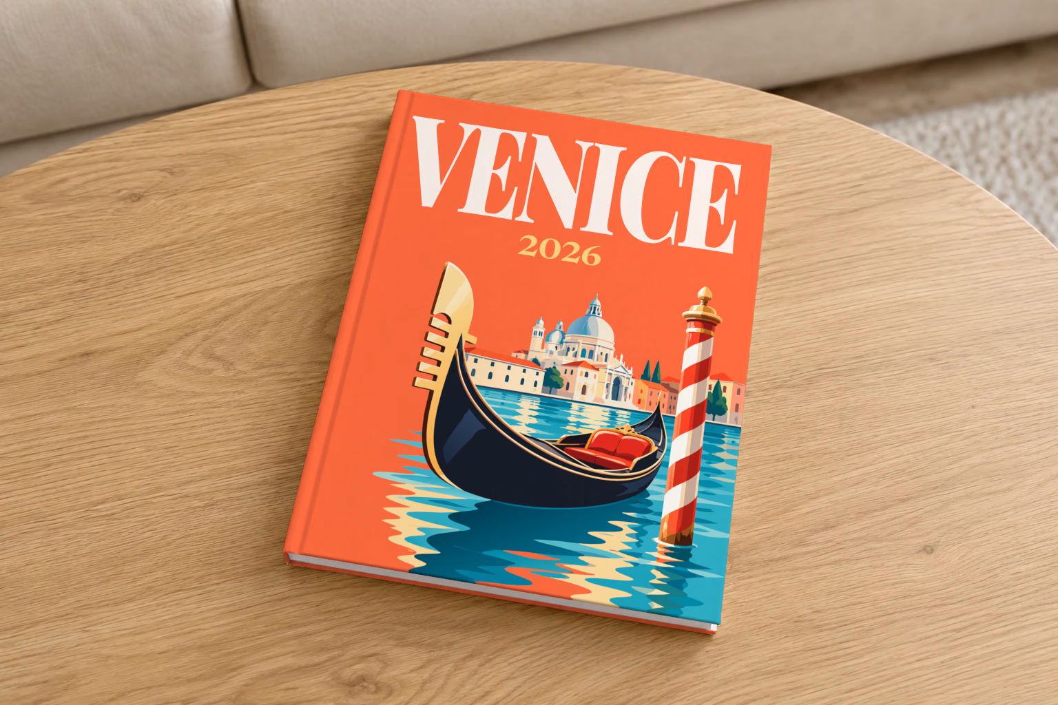 Venice hardcover photo book with the illustrated cover of a gondola, a striped mooring pole and Santa Maria della Salute on red-orange, on a round oak coffee table in a bright living room