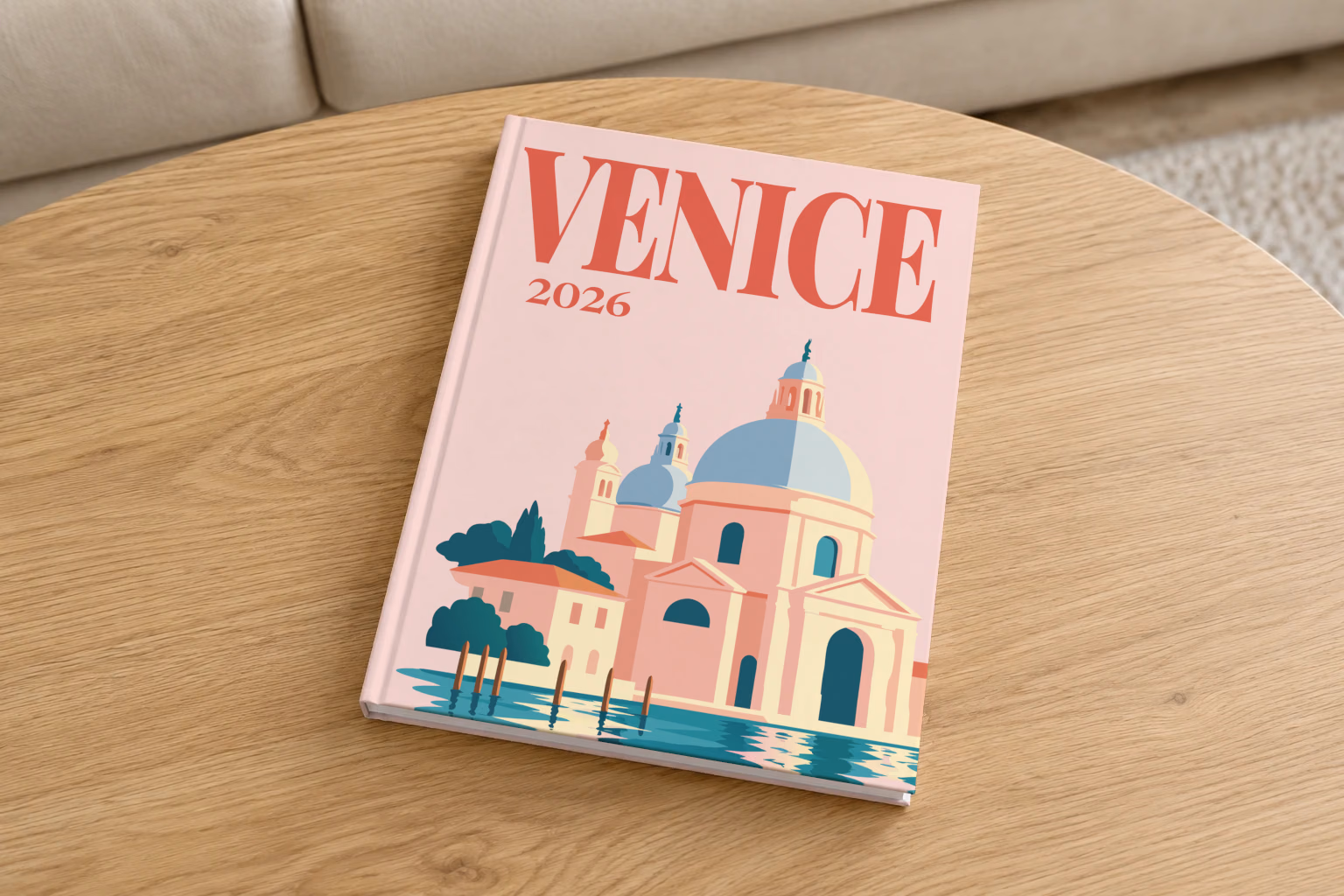 Venice hardcover photo book with the illustrated cover of Santa Maria della Salute on blush pink, on a round oak coffee table in a bright living room