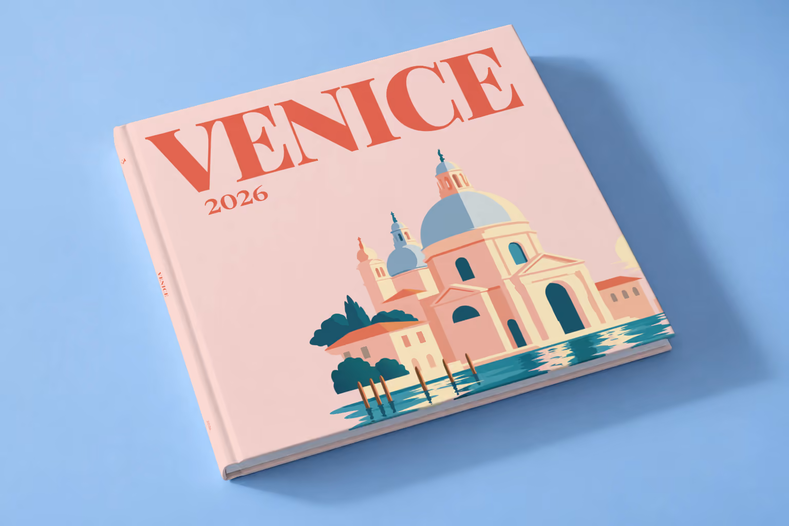 Venice square hardcover photo book with the illustrated cover of Santa Maria della Salute on blush pink, lying on a pale blue studio backdrop