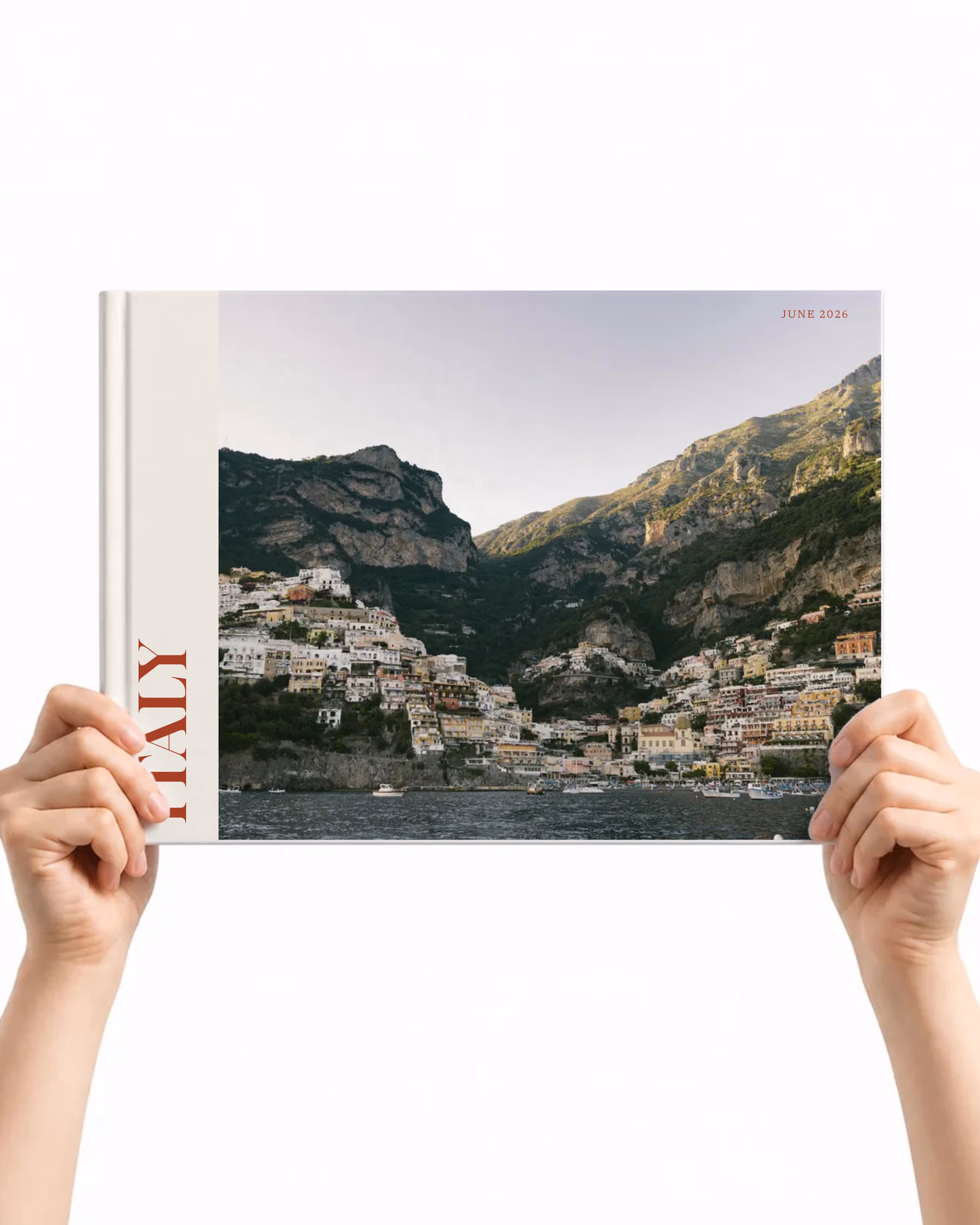 Landscape layflat photo book with the Editorial cover, a photo of a cliffside coastal town beside ITALY in red on a cream panel, held up in two hands