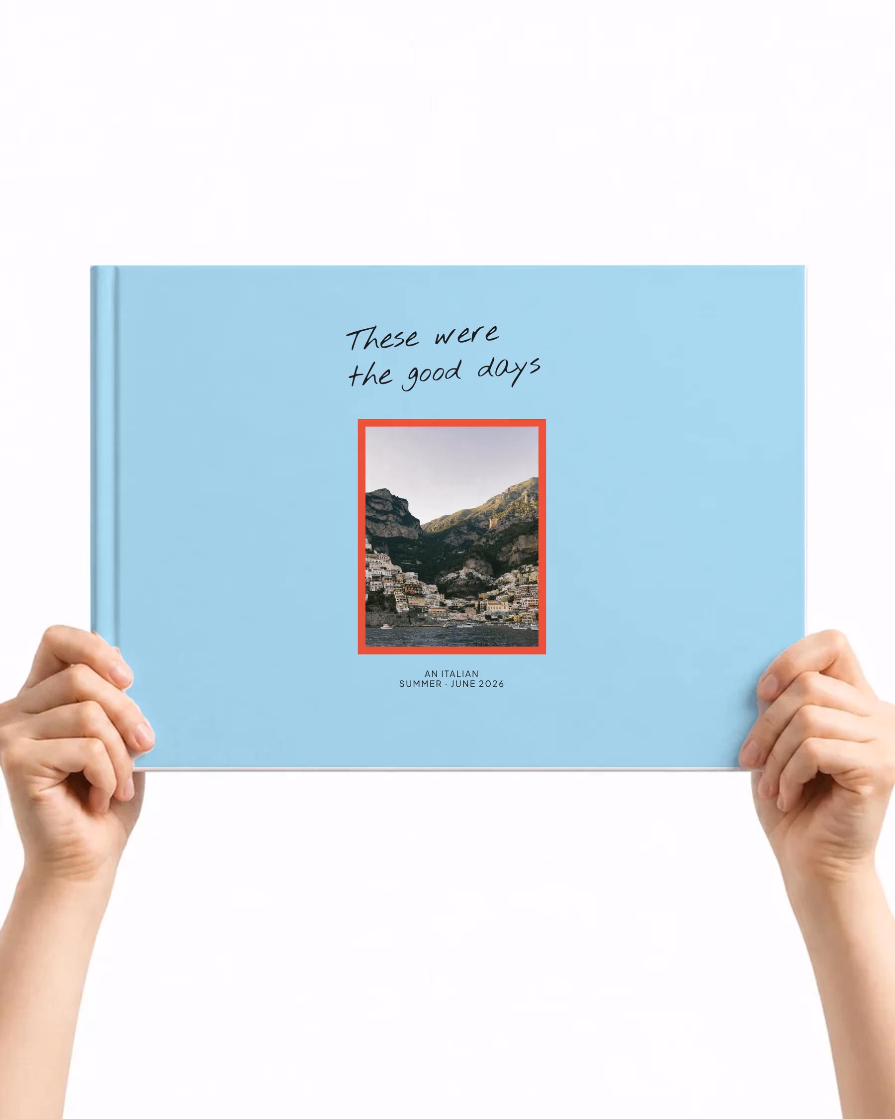 Landscape layflat photo book with the Good days cover, These were the good days handwritten on pale blue above a red-framed photo of a cliffside coastal town, held up in two hands