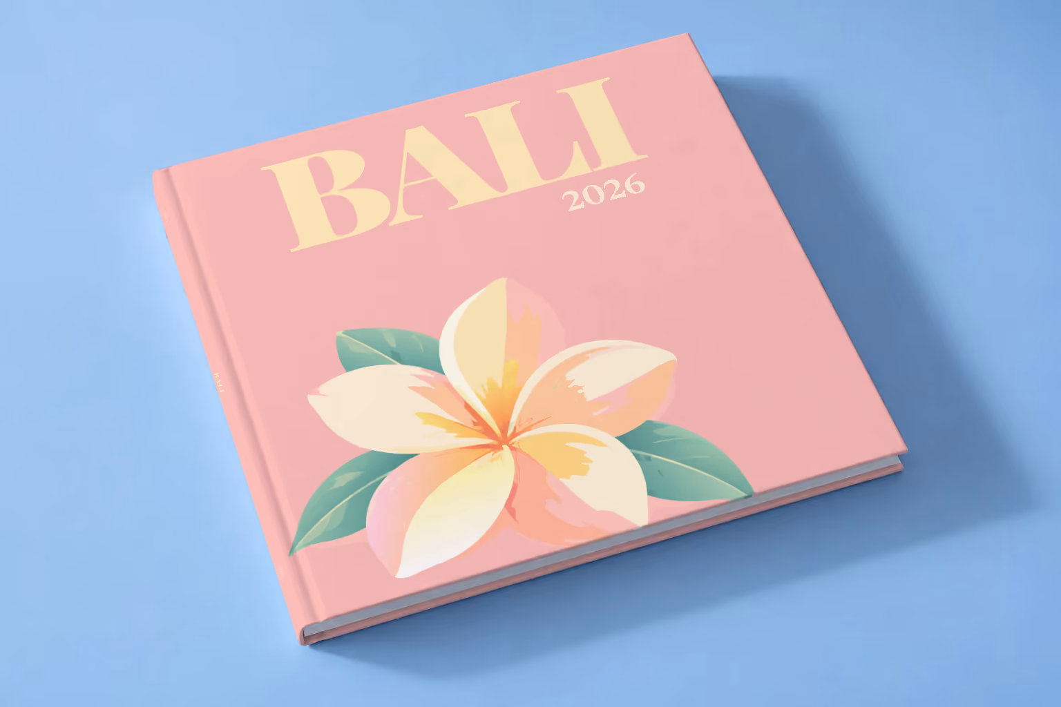 Bali hardcover photo book with an illustrated cover of a frangipani flower, lying on a pale blue studio backdrop