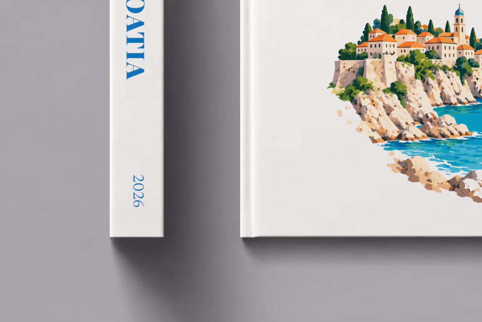 Croatia hardcover photo book with an illustrated cover of an Adriatic old town and sailing boat, shown close up beside its spine on a pale grey studio surface
