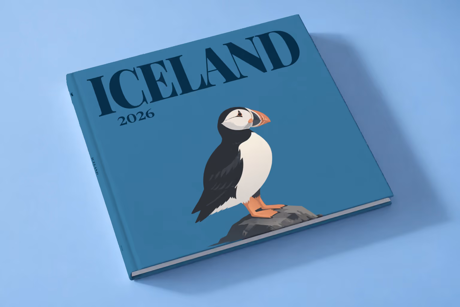 Iceland hardcover photo book with an illustrated cover of a puffin on a rock, lying on a pale blue studio backdrop