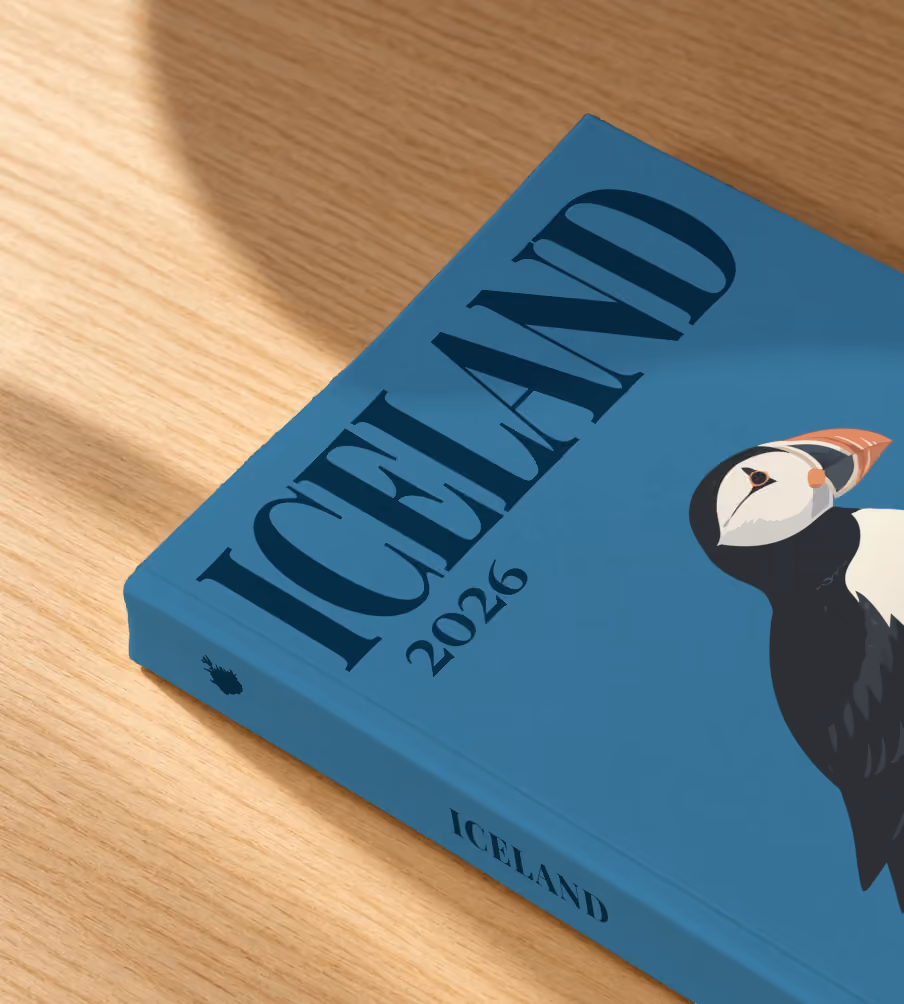 Iceland softcover photo book with an illustrated cover of a puffin on a rock, lying on an oak desk in dappled afternoon sunlight