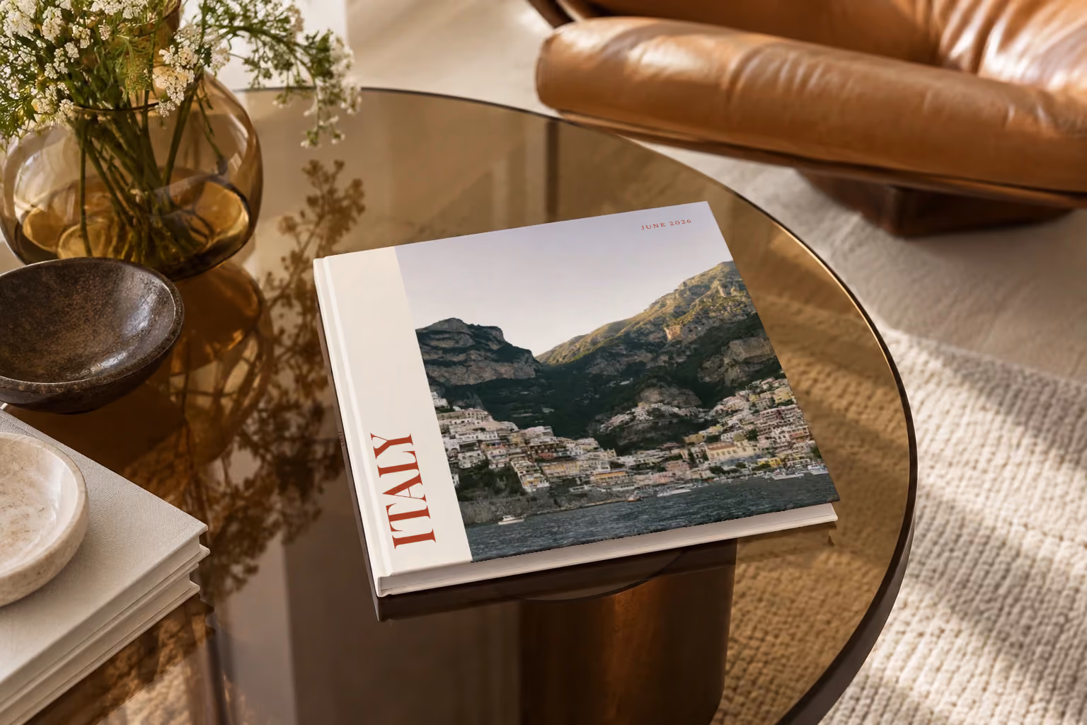 Italy hardcover photo book with the Editorial cover, on a smoked glass coffee table beside a leather armchair in warm afternoon light
