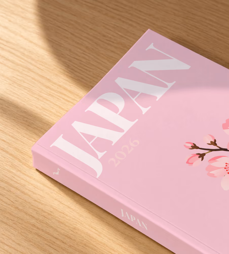 Japan softcover photo book with an illustrated cover of a cherry blossom branch, lying on an oak desk in dappled afternoon sunlight