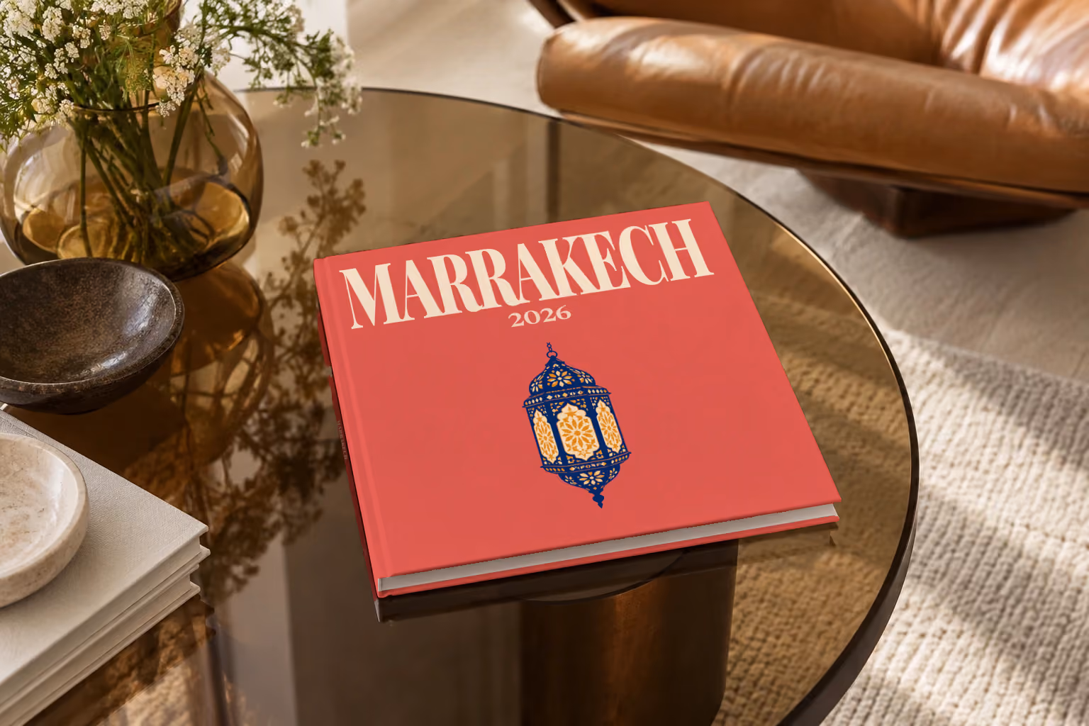 Marrakech hardcover photo book with an illustrated cover of a Moroccan lantern, on a smoked glass coffee table beside a leather armchair in warm afternoon light
