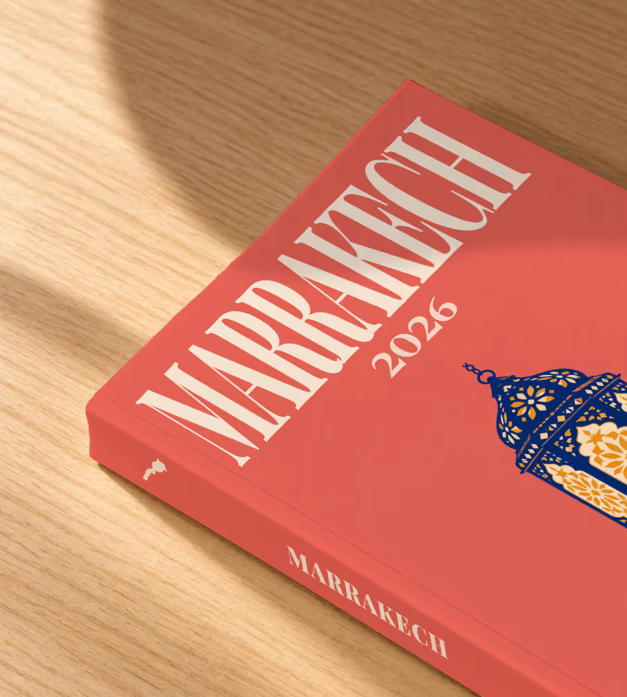 Marrakech softcover photo book with an illustrated cover of a Moroccan lantern, lying on an oak desk in dappled afternoon sunlight