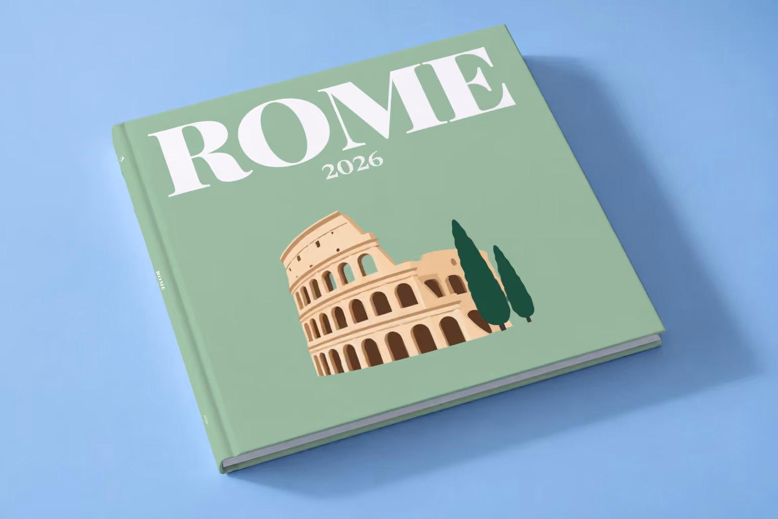 Rome hardcover photo book with an illustrated cover of the Colosseum and cypress trees, lying on a pale blue studio backdrop