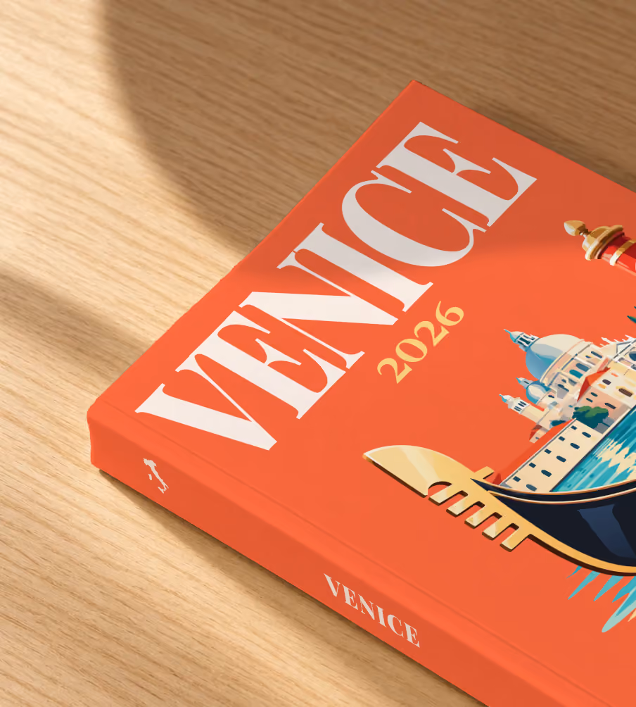 Venice softcover photo book with an illustrated cover of a gondola, a striped mooring pole and Santa Maria della Salute, lying on an oak desk in dappled afternoon sunlight