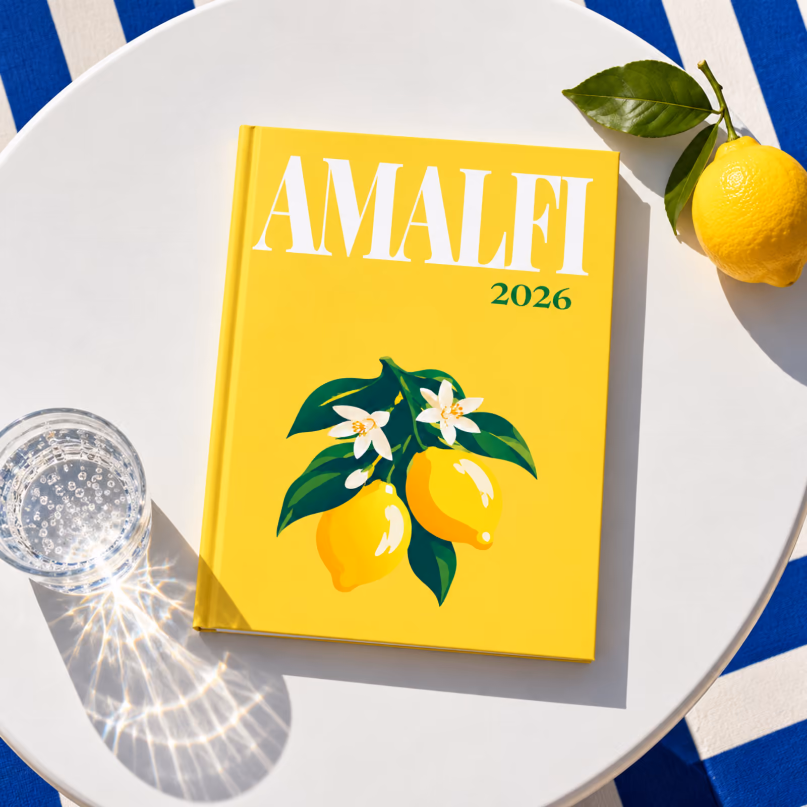 A yellow Amalfi travel photo book illustrated with lemons, on a white poolside table beside a fresh lemon