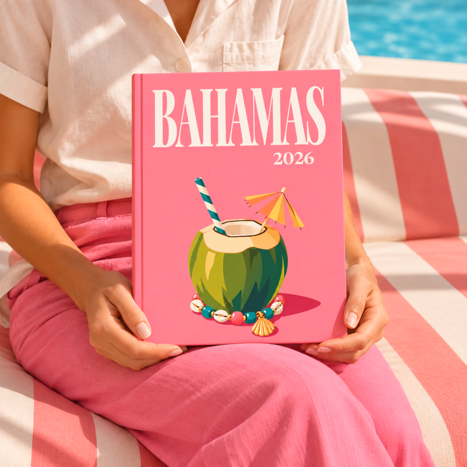 A woman on a pink striped sofa holding a Bahamas travel photo book with an illustrated coconut drink