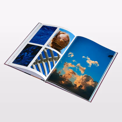 Open hardcover photo book with blue tile, portrait and cloudy sky photos printed across both pages