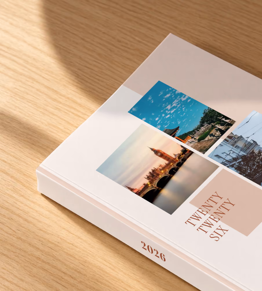 Editorial II year in review softcover photo book, a blush editorial cover with three travel photos, lying on an oak desk in dappled afternoon sunlight