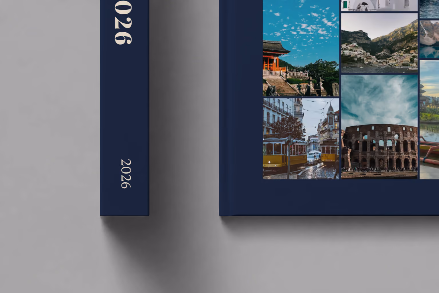 Mosaic III year in review hardcover photo book, a navy cover with a mosaic of travel photos, shown close up beside its spine on a pale grey studio surface