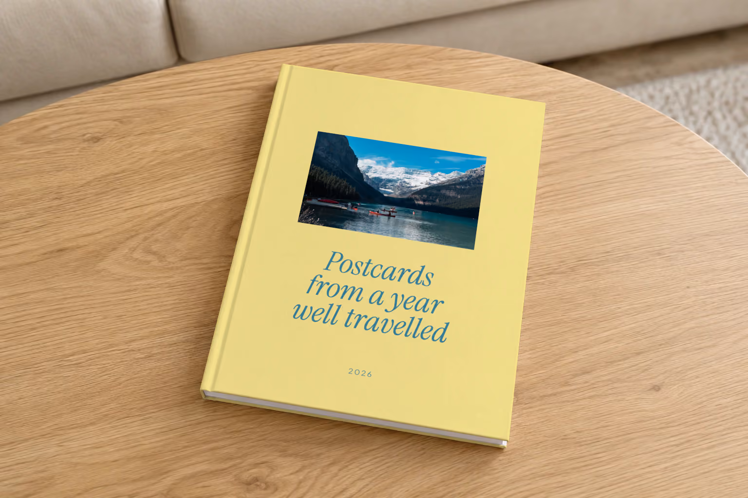 Postcards year in review hardcover photo book, a yellow cover reading Postcards from a year well travelled, on a round oak coffee table in a bright living room