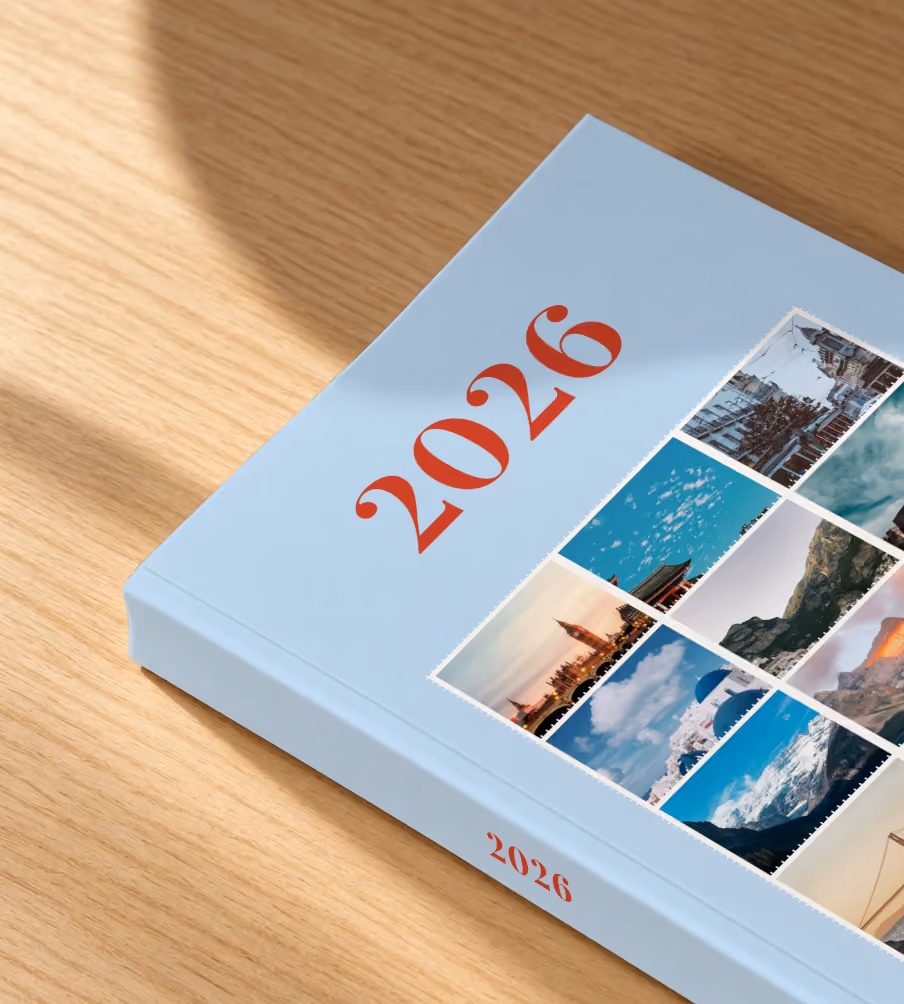 Stamps I year in review softcover photo book, a pale blue cover of travel photo stamps, lying on an oak desk in dappled afternoon sunlight
