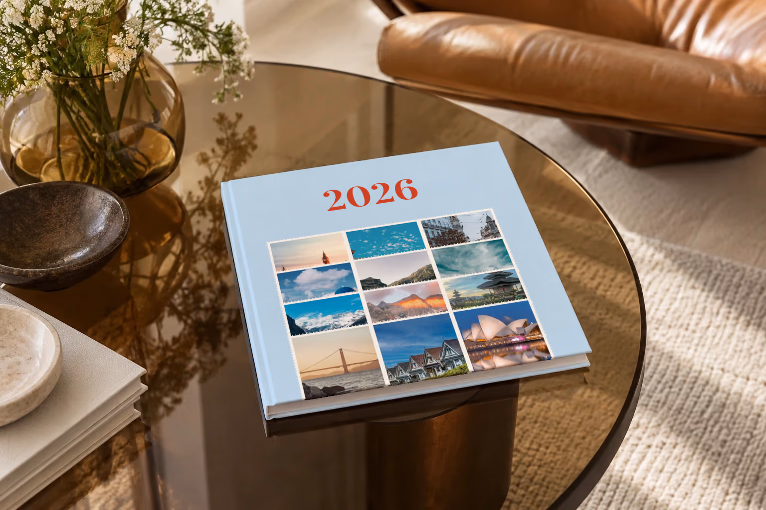 Stamps I year in review square hardcover photo book, a pale blue cover of travel photo stamps, on a smoked glass coffee table beside a leather armchair in warm afternoon light