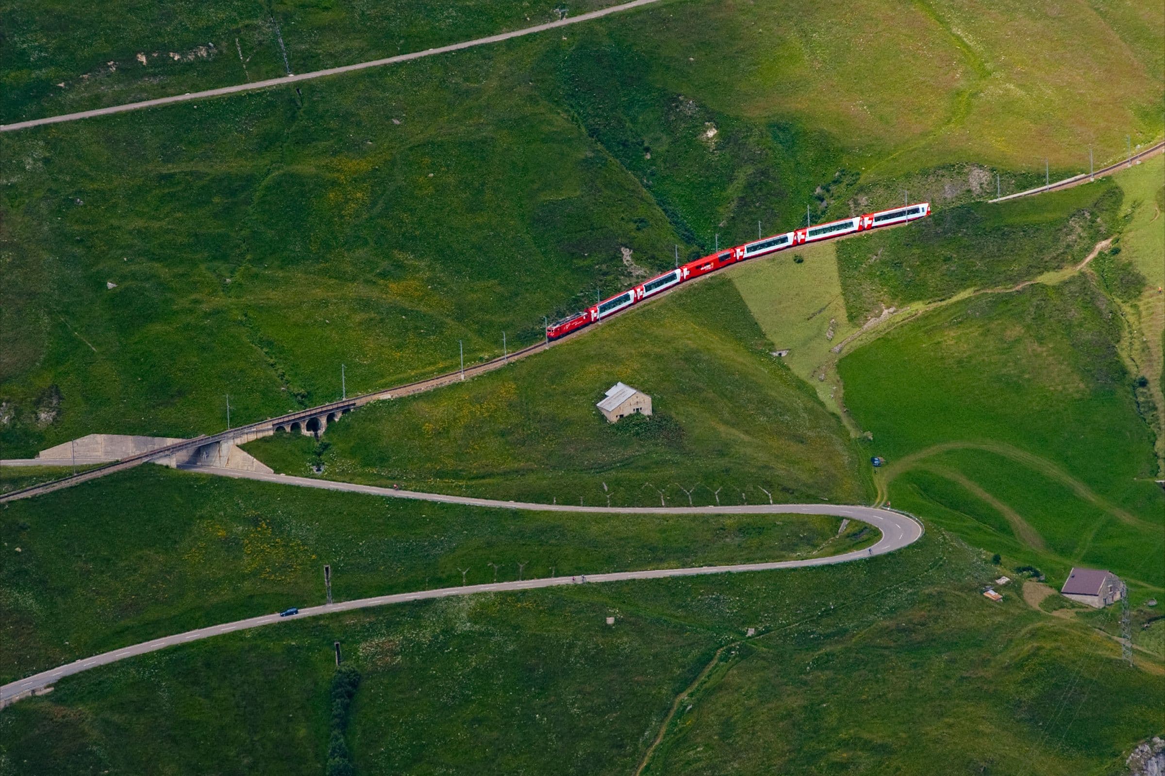 A winding mountain road beside a red passenger train
