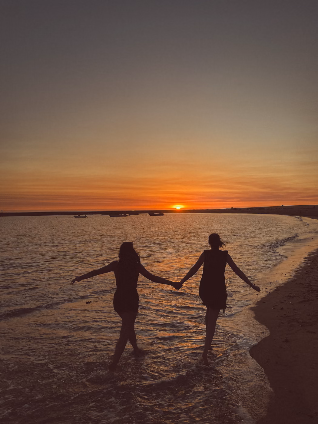 Two friends holding hands at sunset on the beach