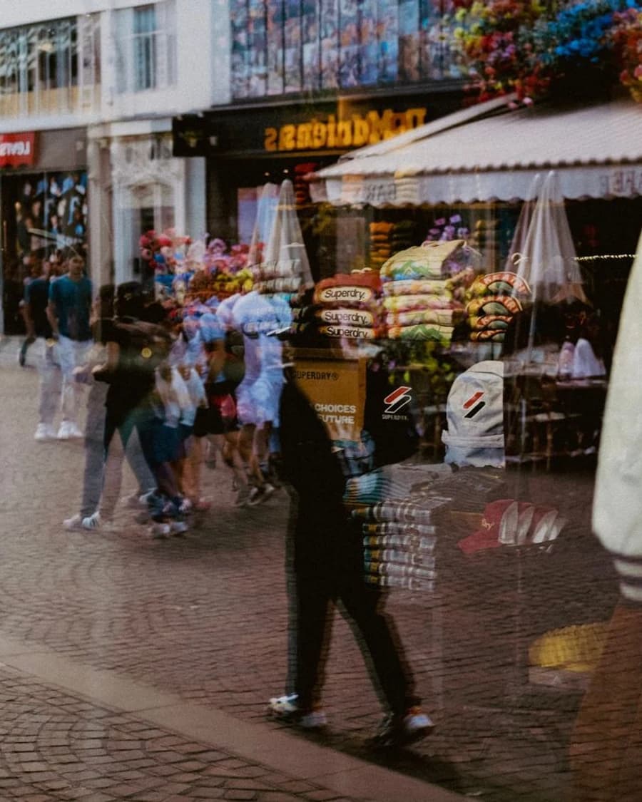 Layered reflection of pedestrians and a colourful shop window