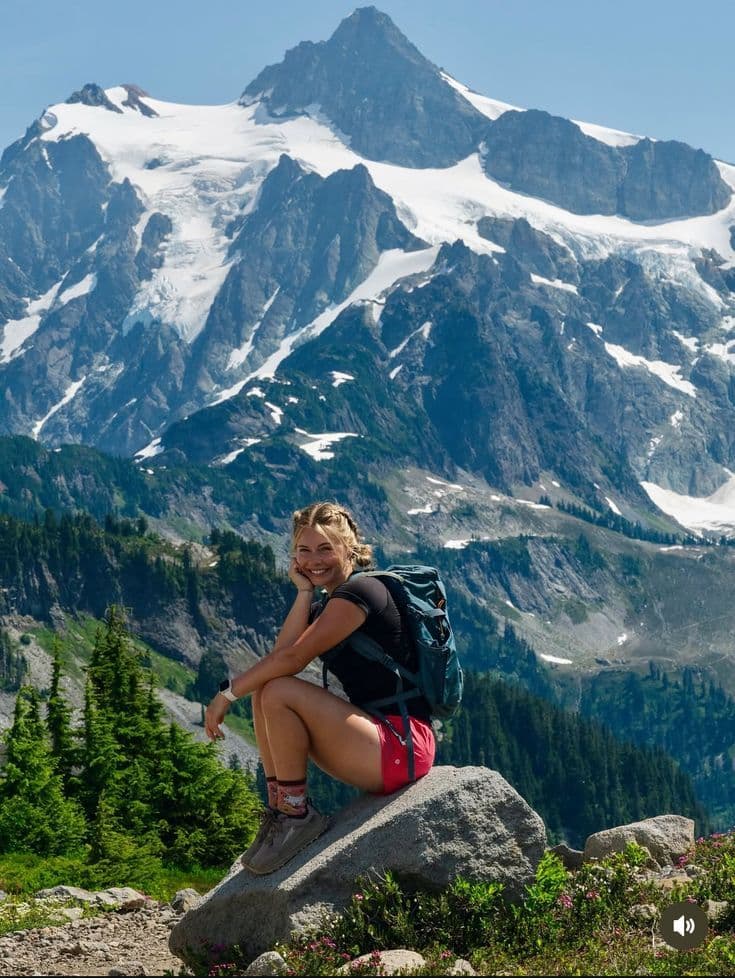 Backpacker resting beside a mountain trail with snowy peaks behind her