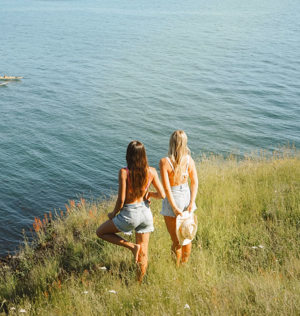 Two friends walking through long grass above the sea on a trip together