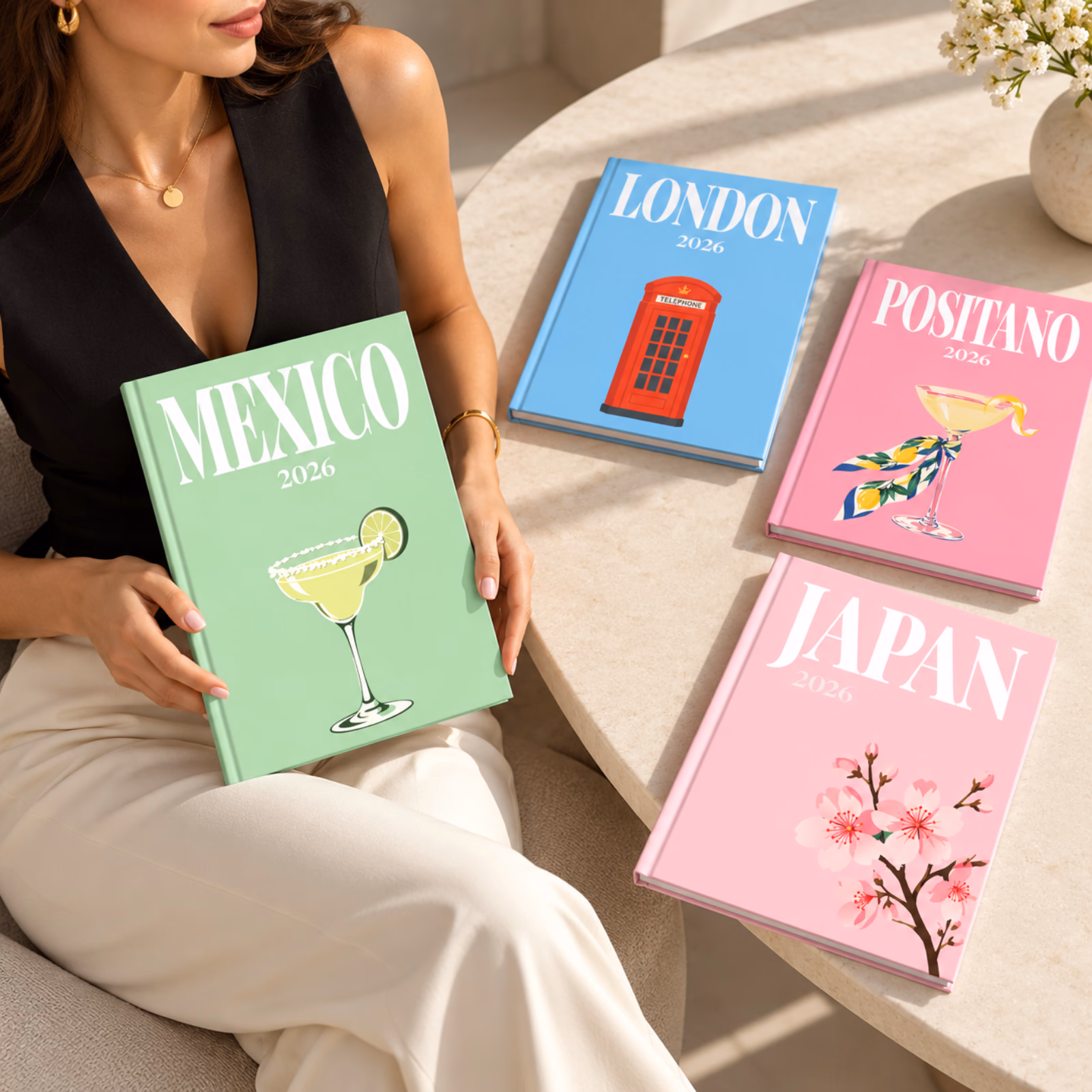 A woman on a sofa holding a green Mexico travel photo book, with London, Positano and Japan photo books on the table beside her